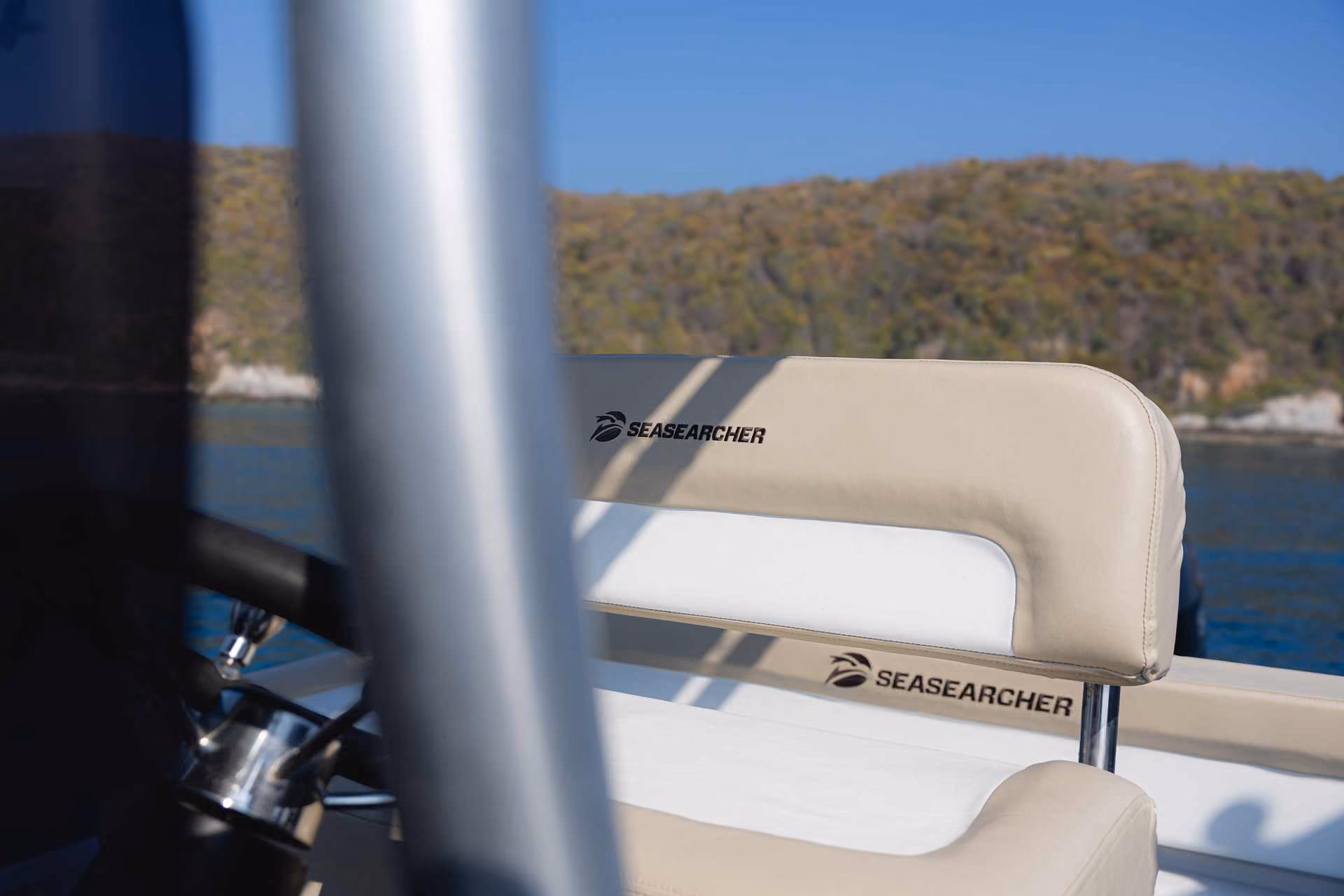 Beige and white cushioned boat seat with SEASEARCHER logo and blurred background of water and hillside.
