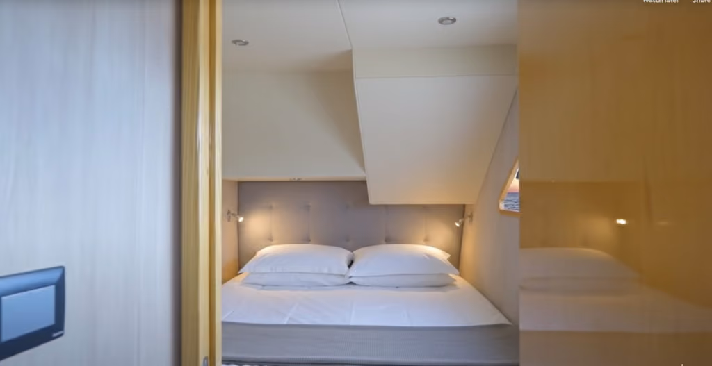 Compact bedroom with a double bed featuring white bedding, two pillows, gray tufted headboard, and reading lights on each side.