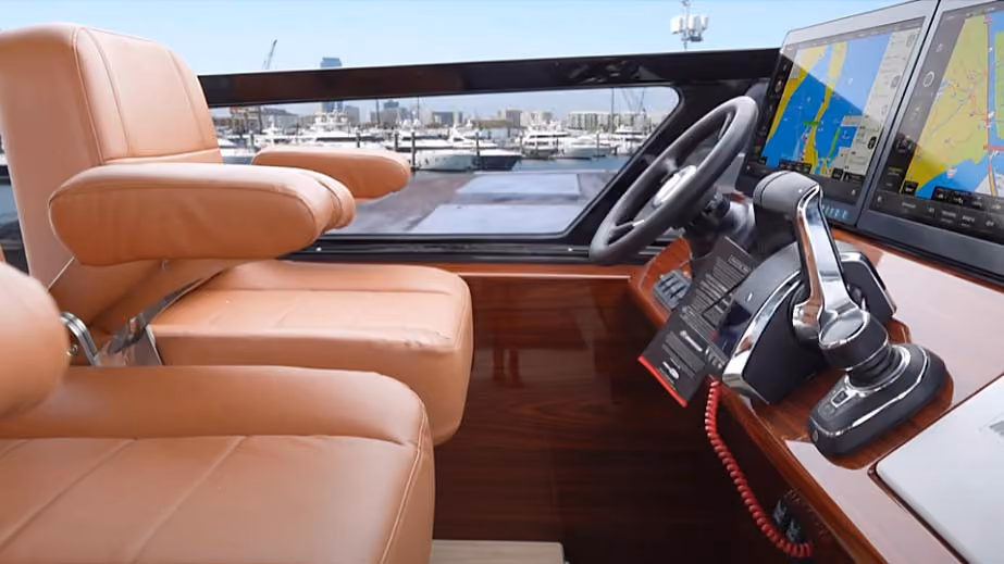 Interior of a boat cockpit showing two beige leather pilot seats, a steering wheel, and dual navigation screens displaying marine charts.