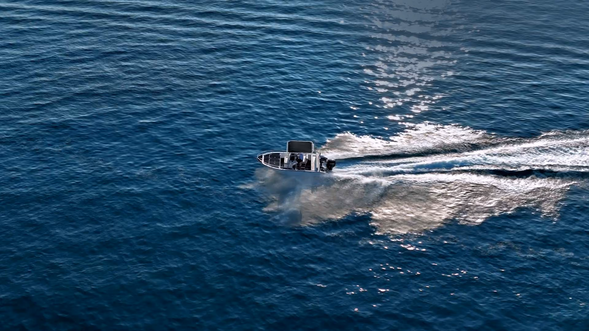 A small motorboat speeding on calm blue ocean water creating white wake trails.