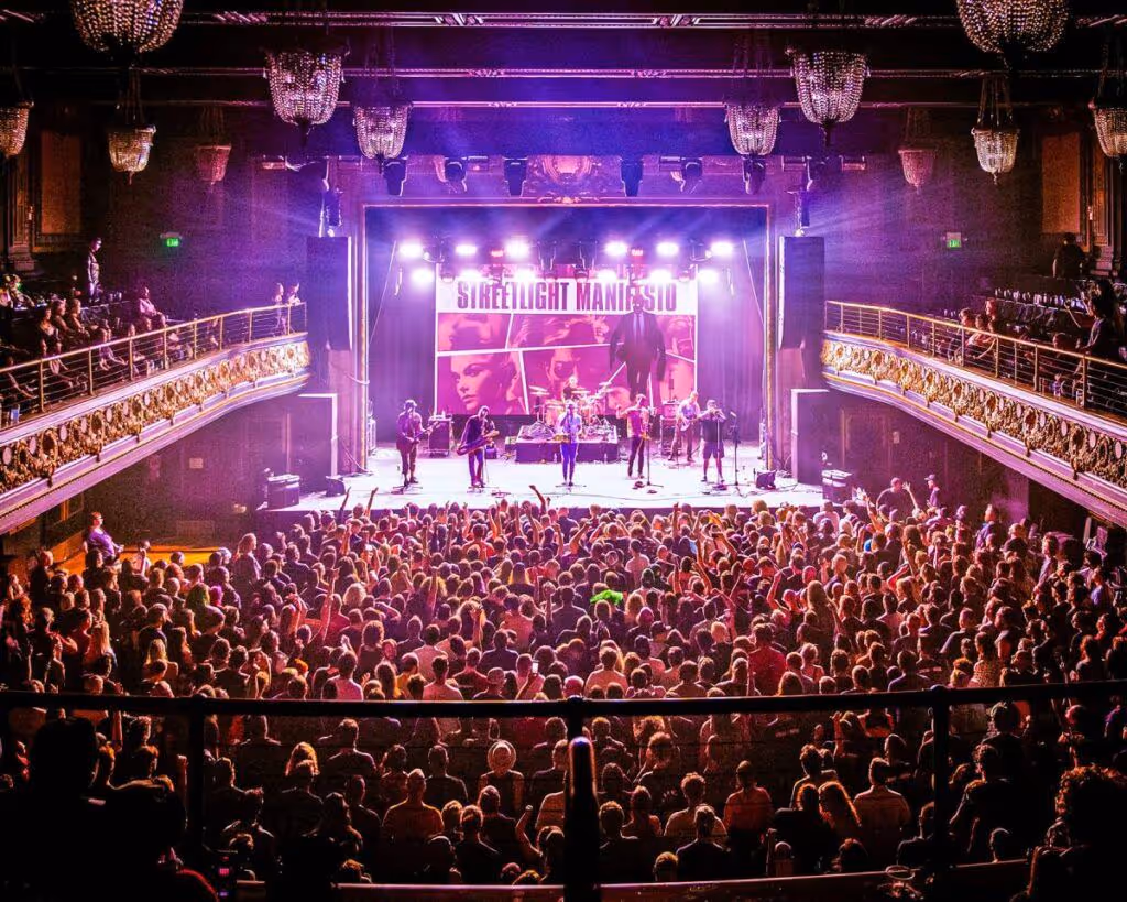 Full theatre crowd in front of a lit stage during a show