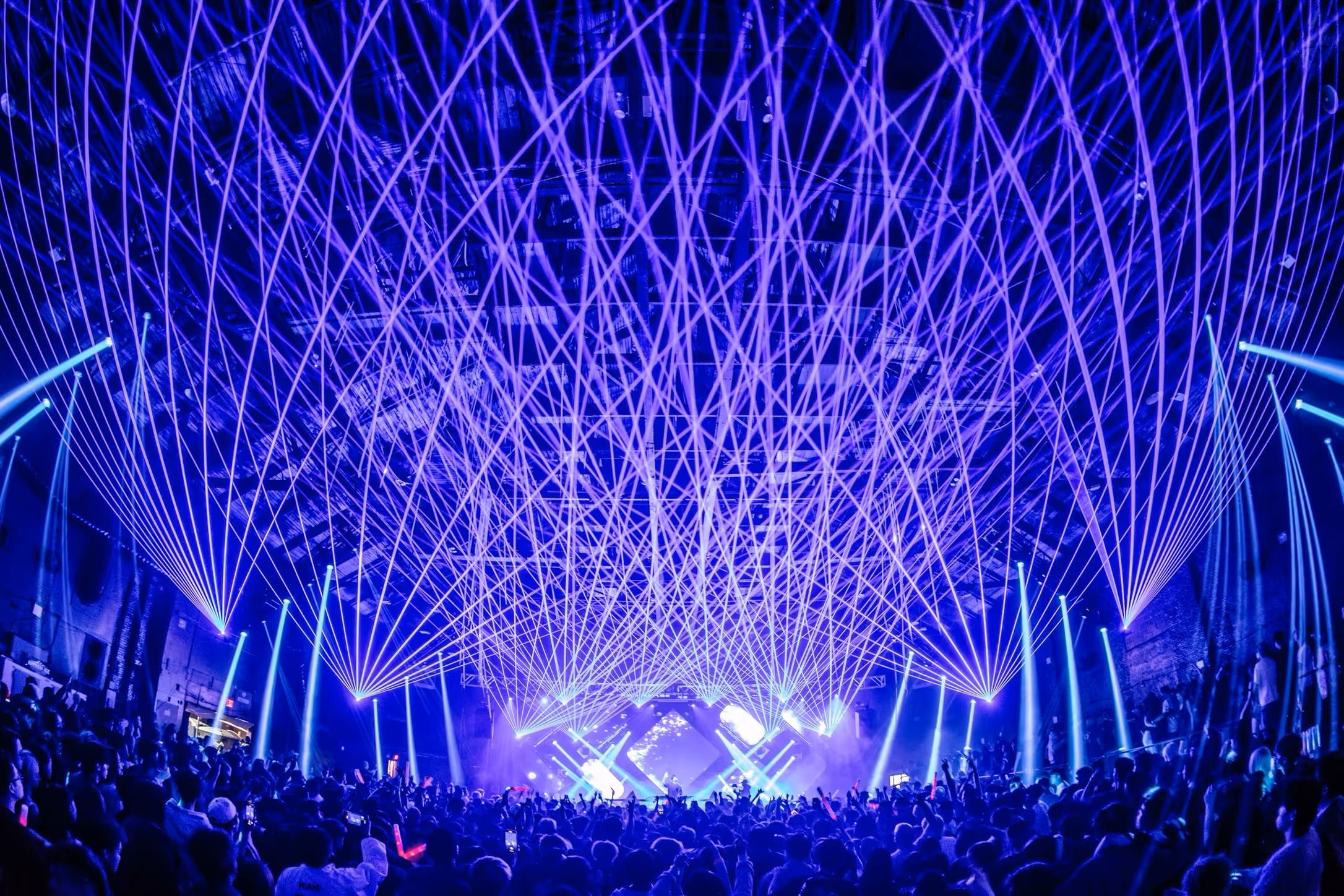 Fan of blue beams over a full arena crowd from a downstage lighting rig