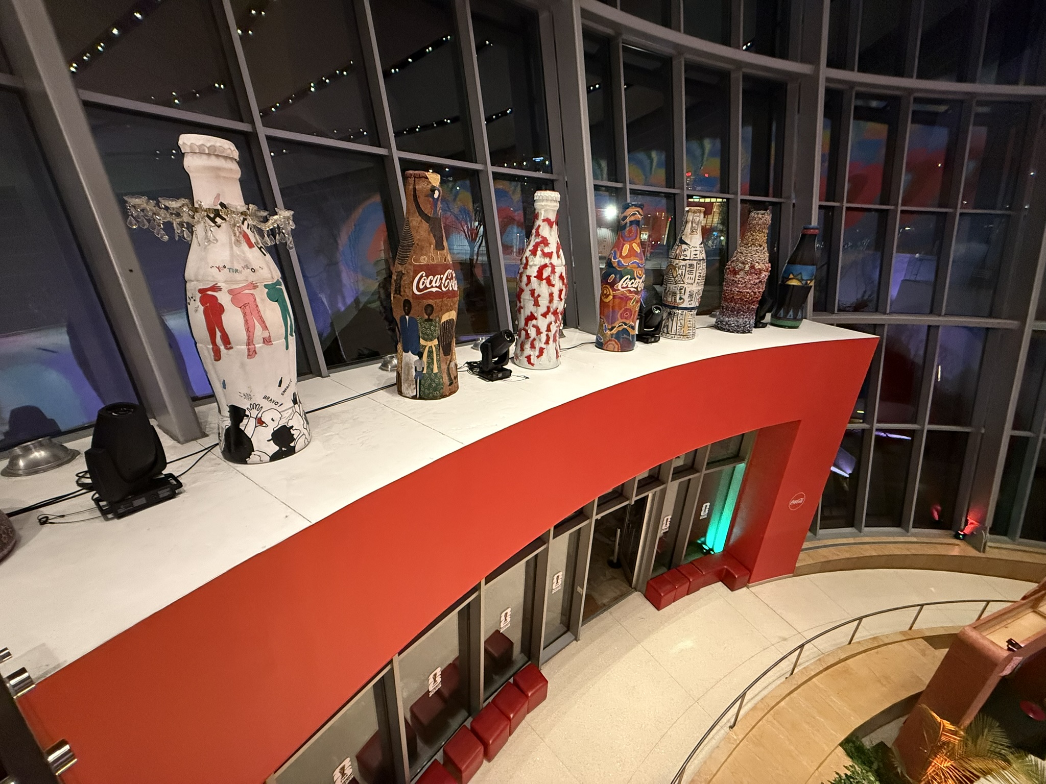 Moving lights staged on a balcony counter beside decorated Coca-Cola bottle sculptures