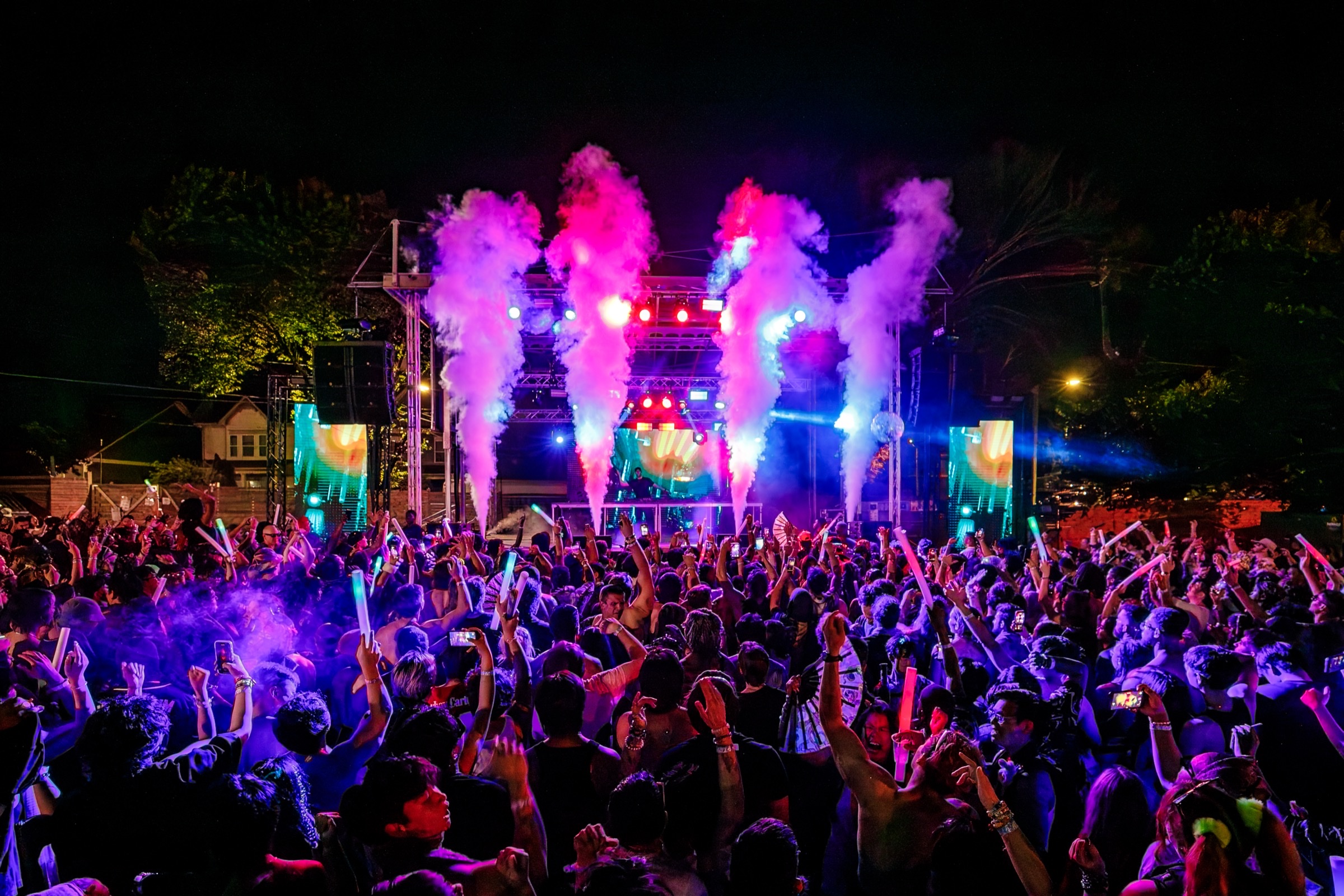 Night crowd with raised arms as four CO2 jets fire over the stage