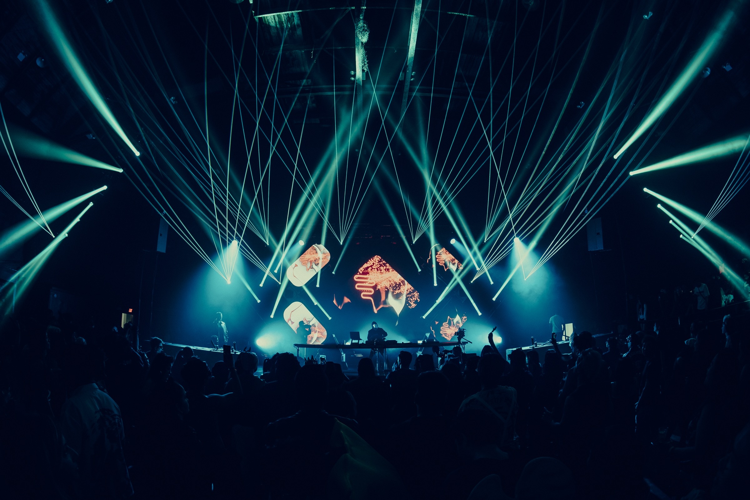 Concert stage with teal beams crossing in haze over a segmented LED wall
