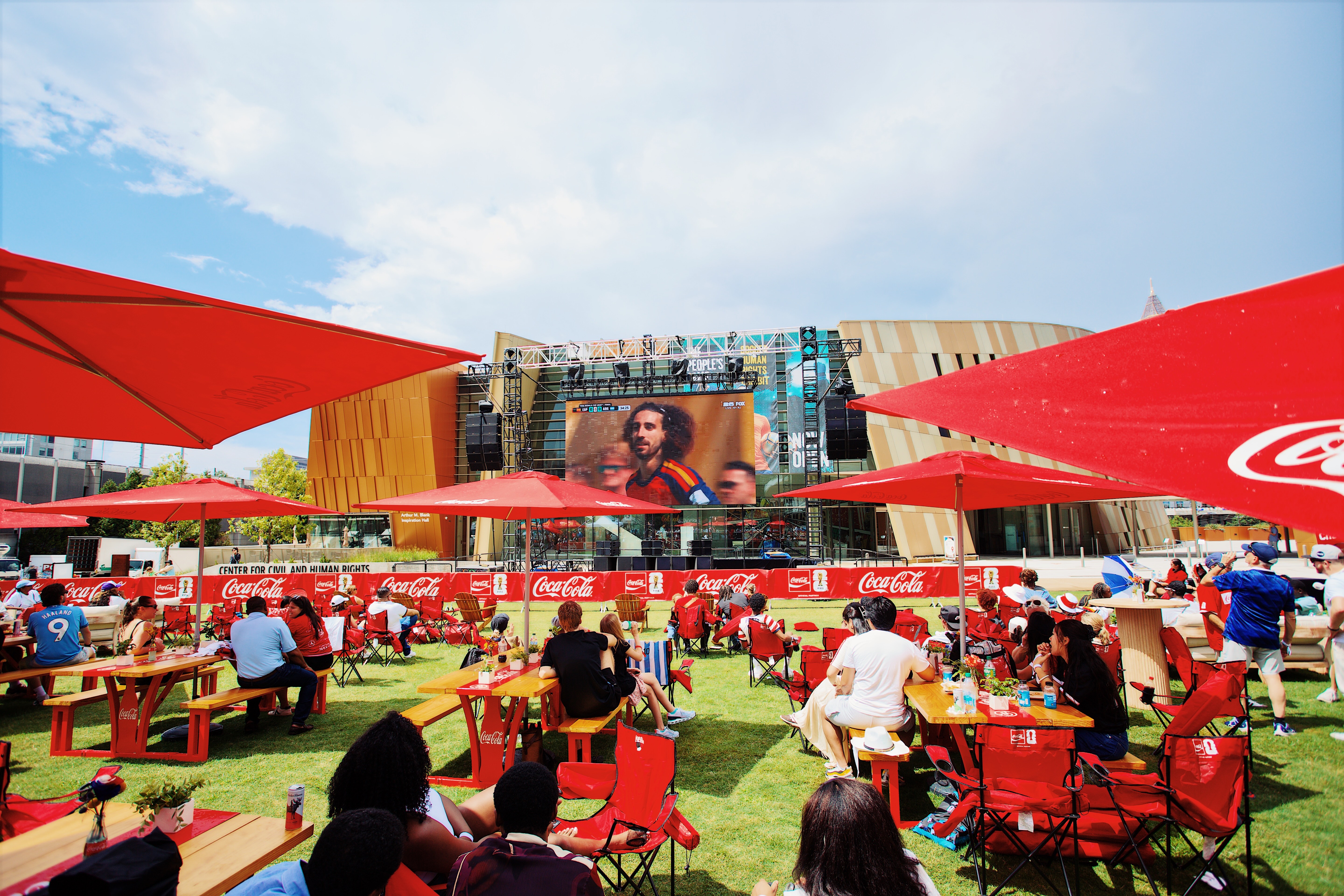 Outdoor watch party on a lawn with a scaffold mounted LED screen and shaded seating
