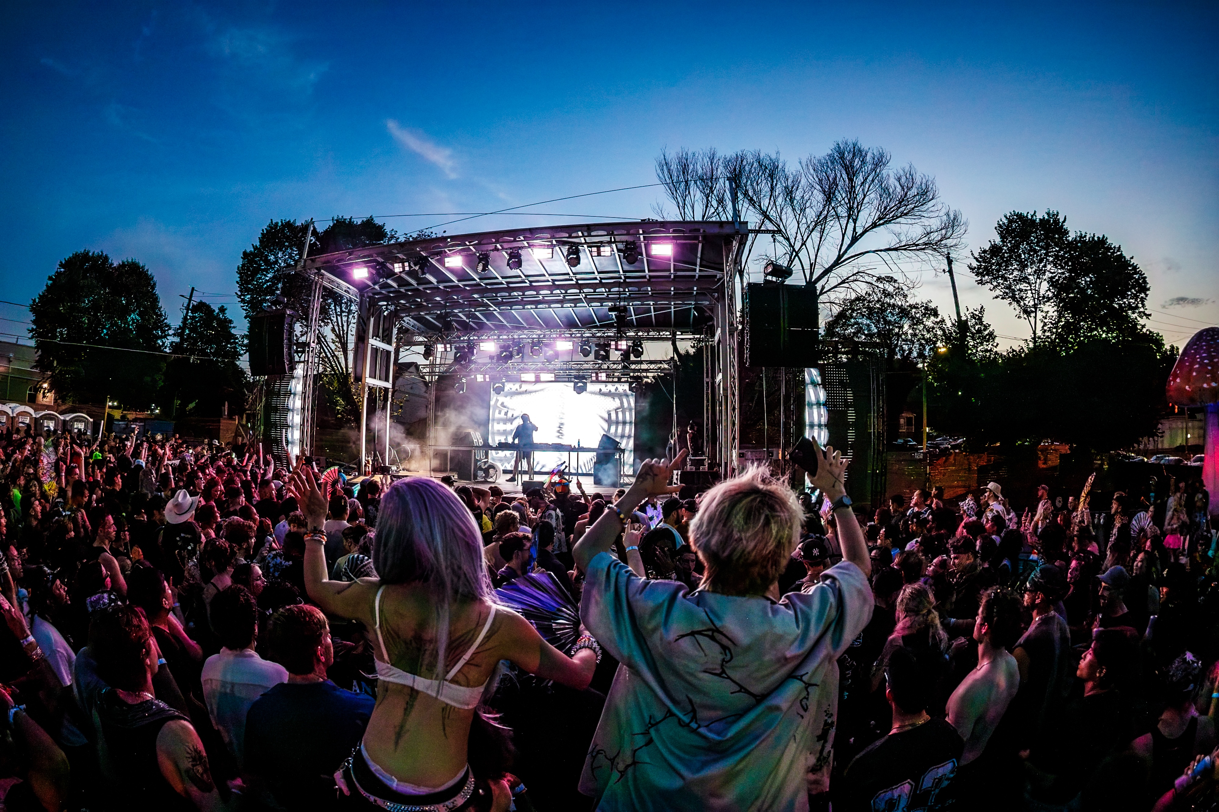 Crowd at dusk facing a festival stage washed in magenta