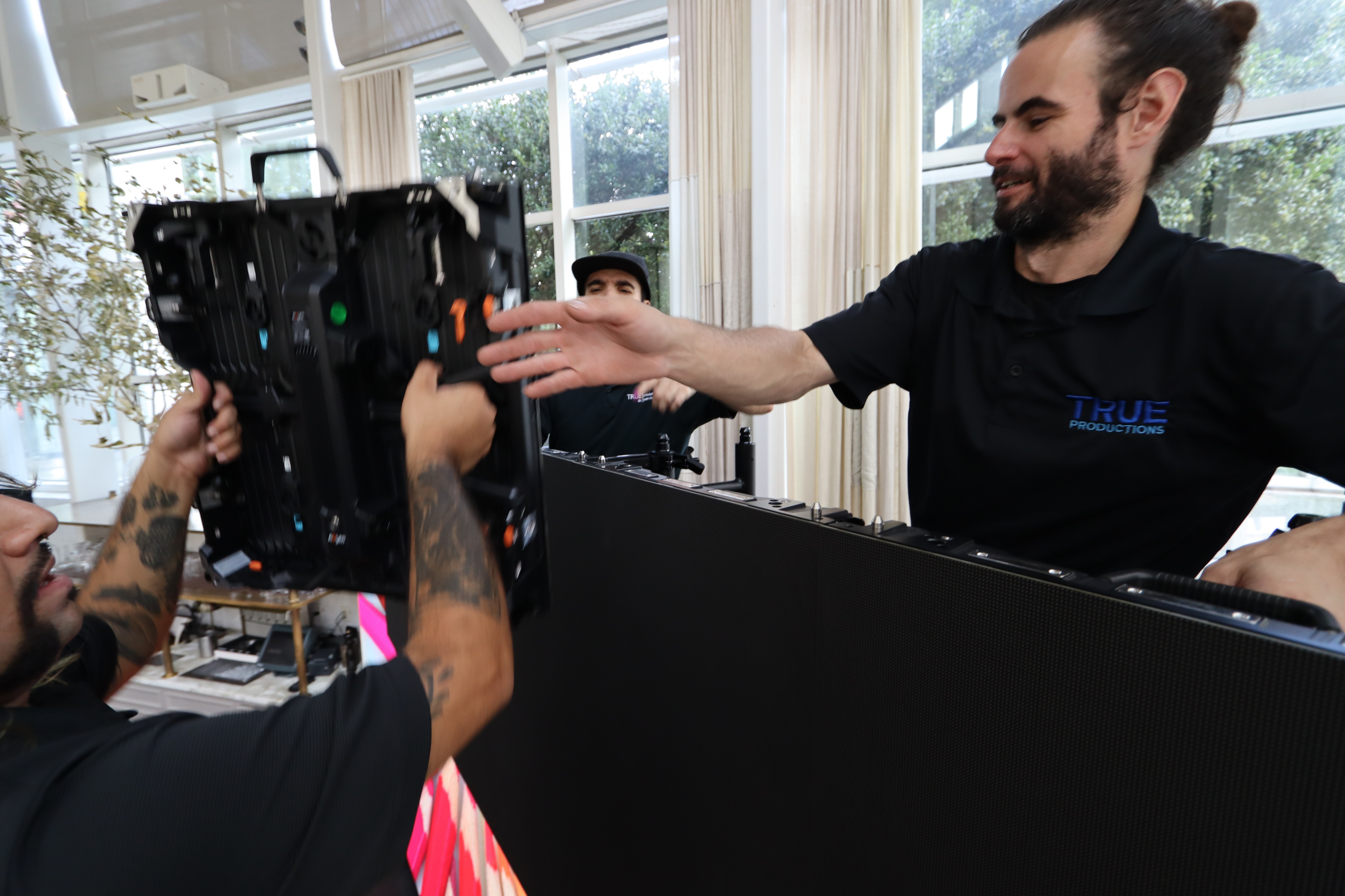 Two True Productions technicians handing off an LED panel while building a video wall in a daylit room