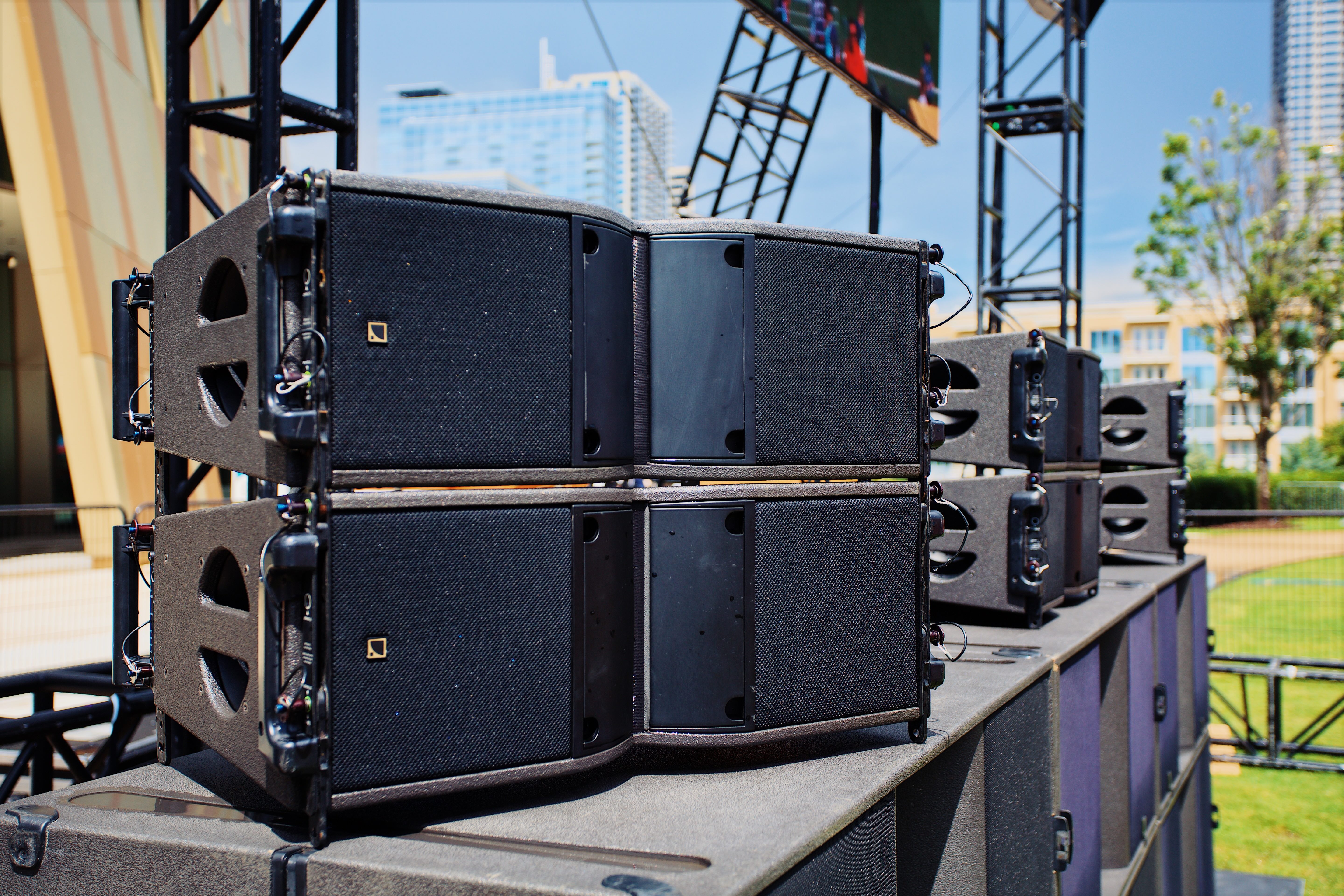 Ground stacked line array cabinets on an outdoor stage deck with a city skyline behind