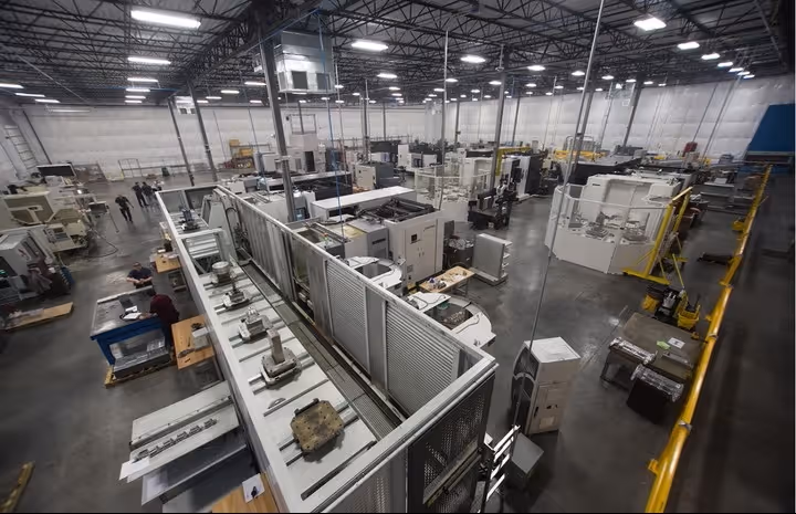 Wide view of a clean, organized industrial workshop with various machines, workbenches, and workers in a spacious warehouse.