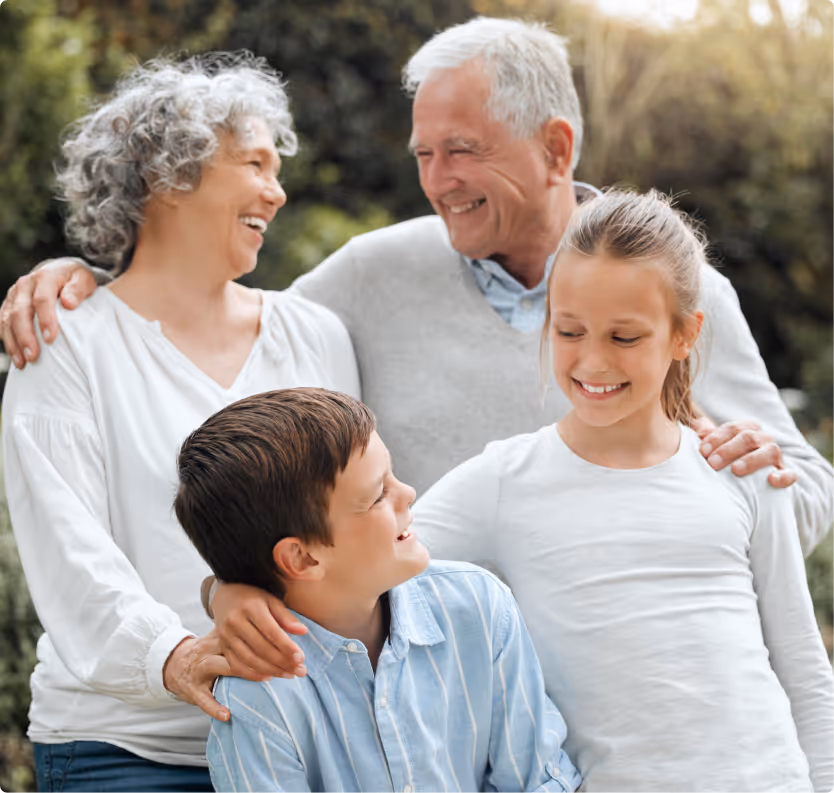 Smiling elderly couple with two happy children outdoors in a garden.