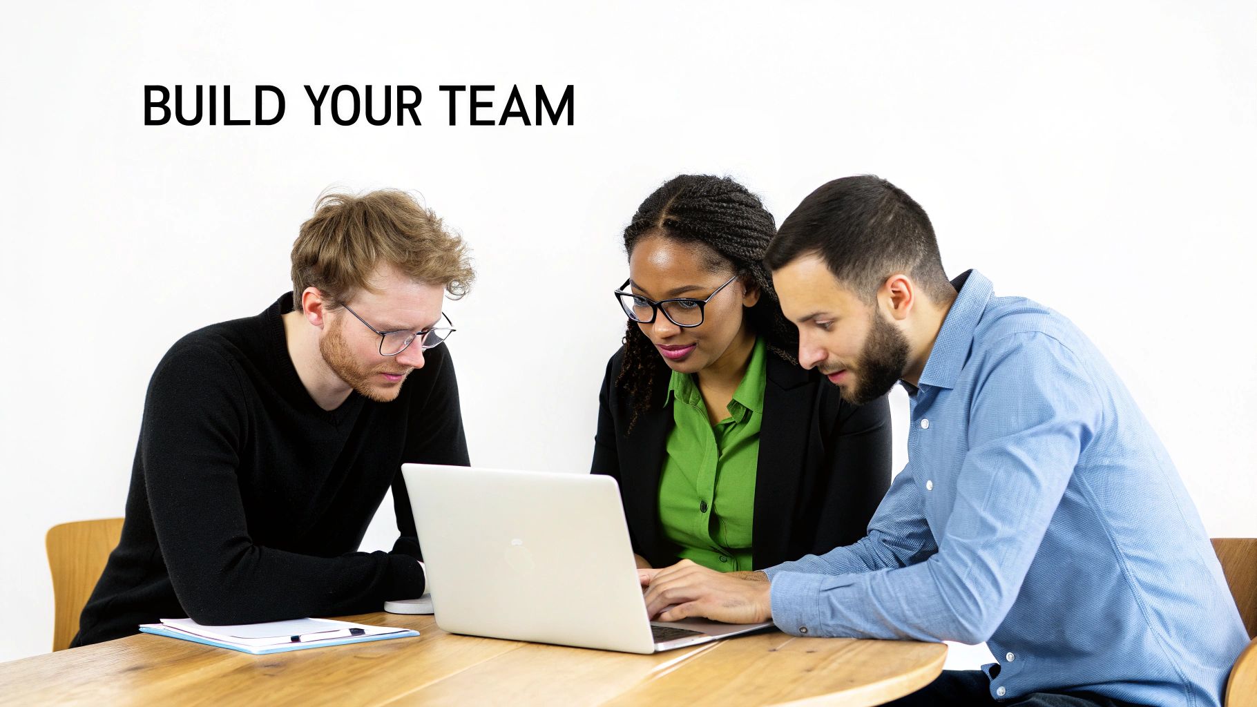 A diverse team of three colleagues collaborating around a laptop on a wooden table.