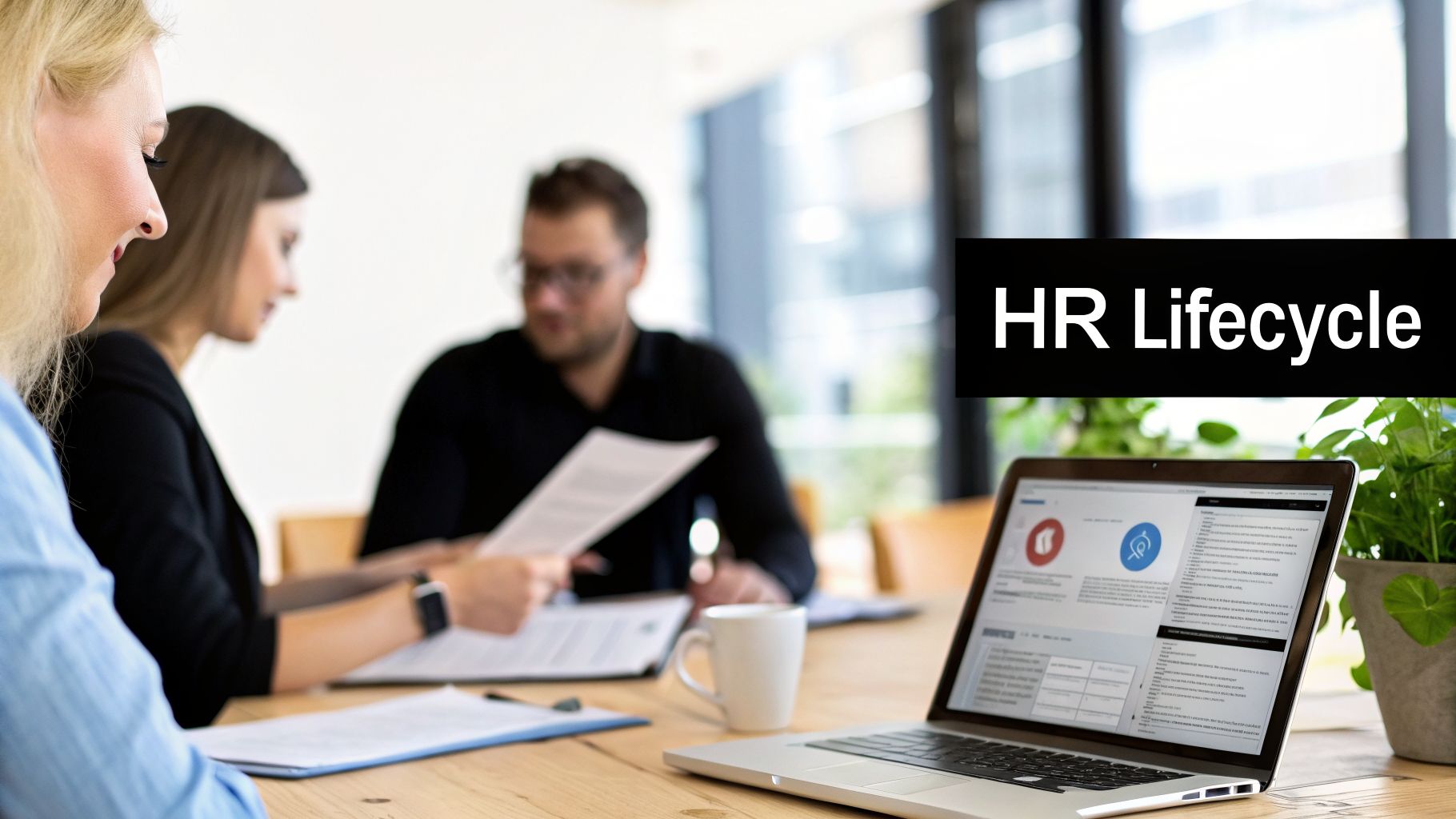 Business professionals reviewing HR lifecycle on a laptop and documents during a meeting in an office.
