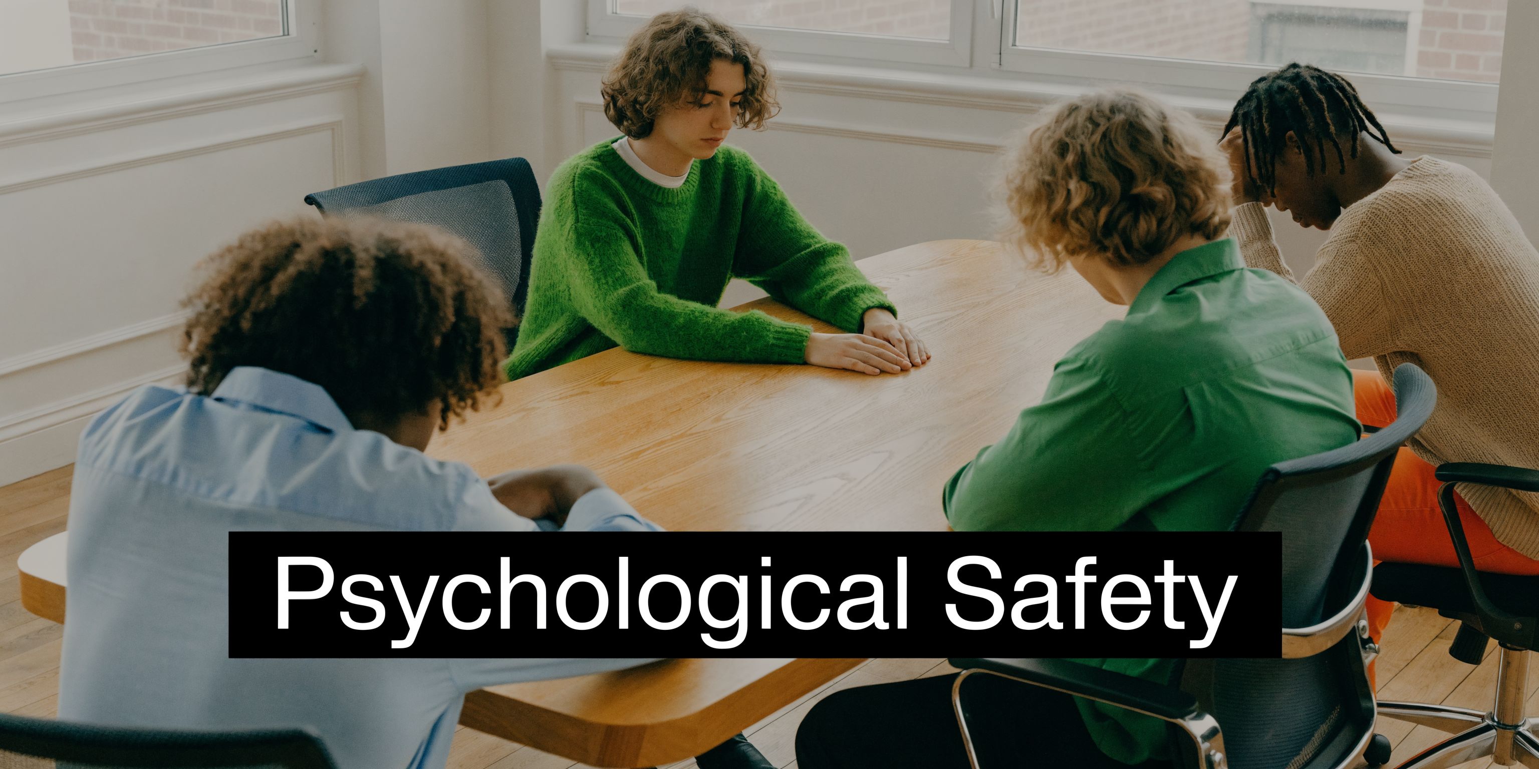 A diverse group of four people sitting at a wooden table looking stressed or disappointed together.
