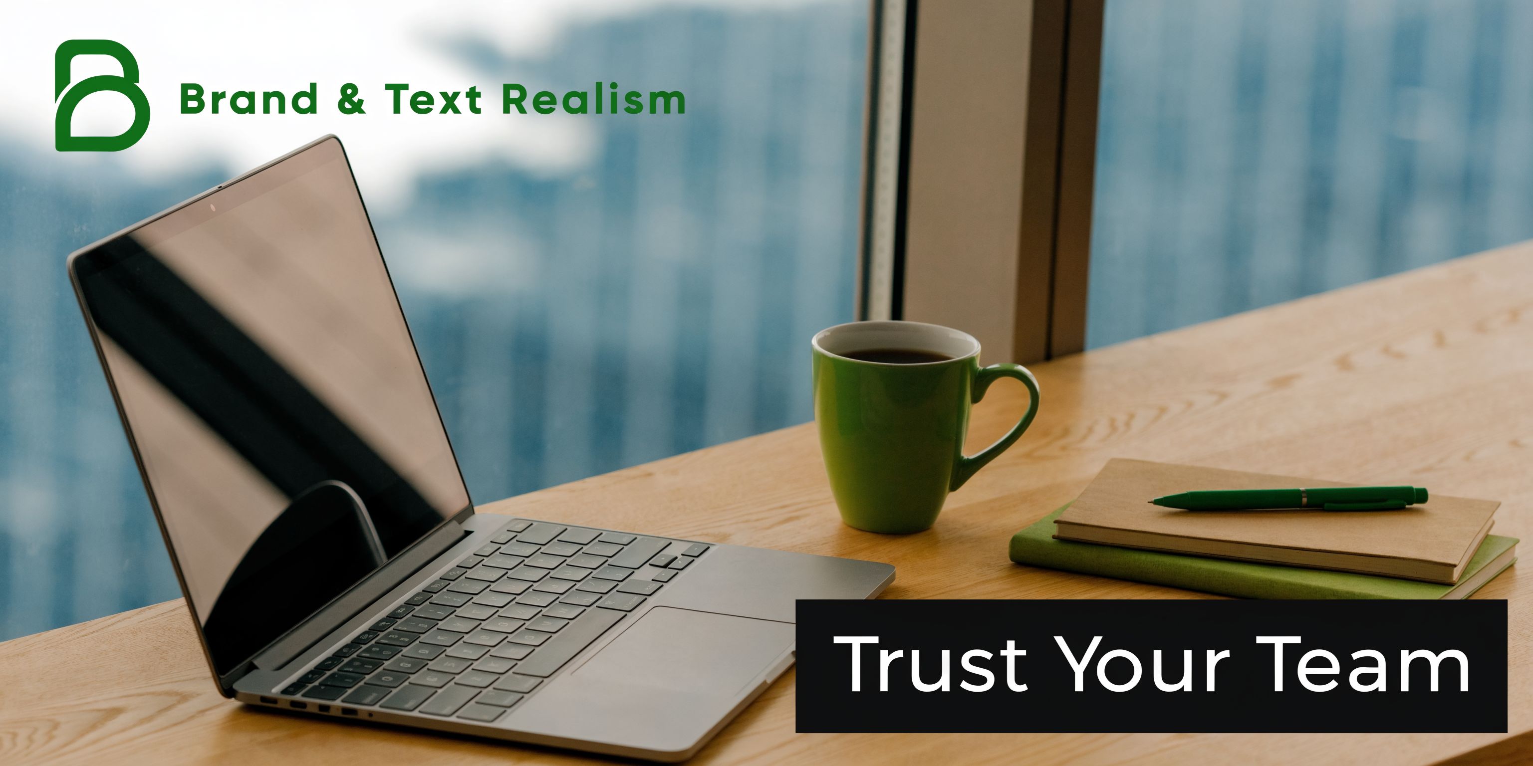 A modern laptop, a green mug, and a notebook on a wooden desk near a window.