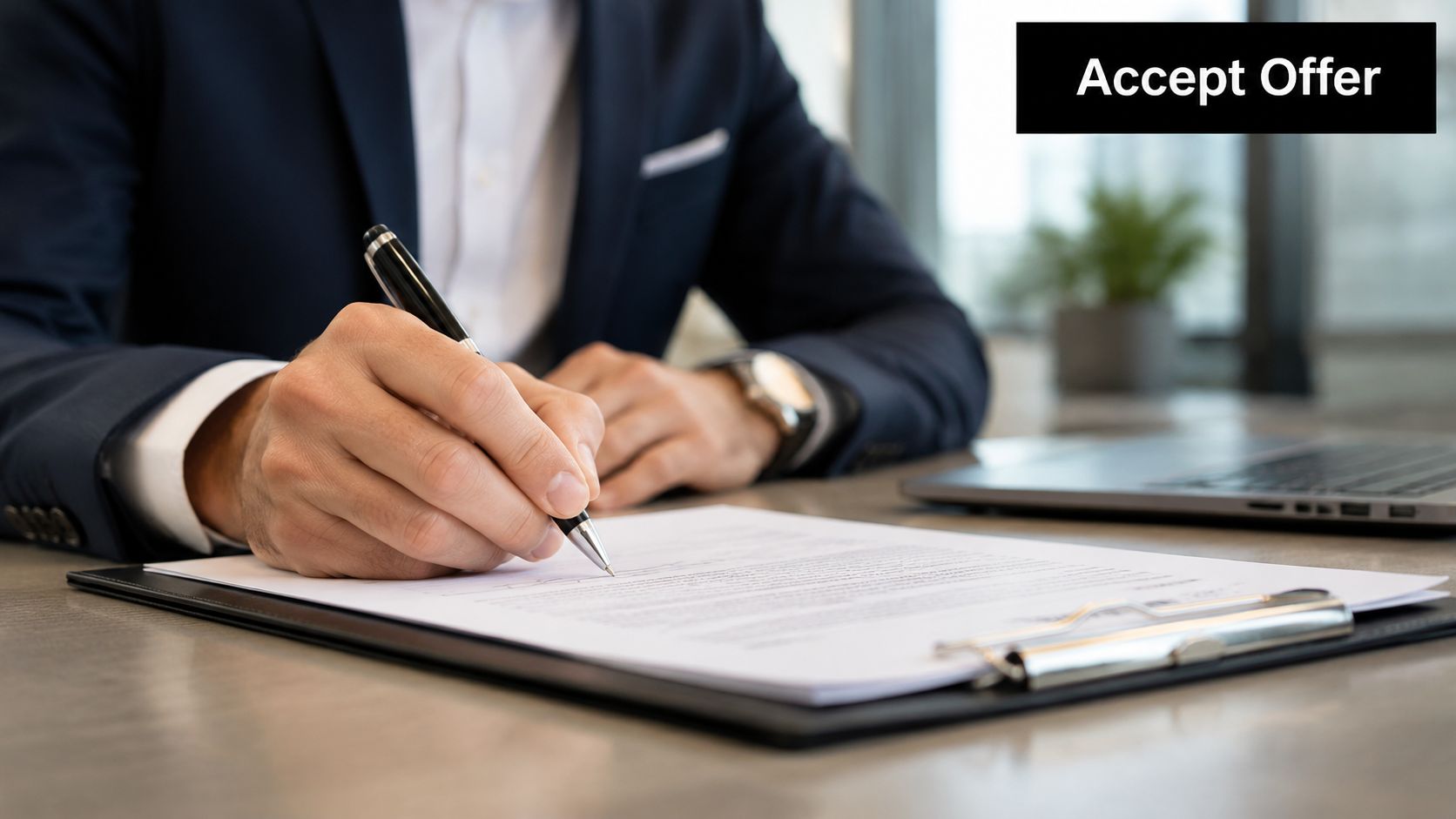 A professional in a business suit signing a formal employment contract at a desk with a laptop.