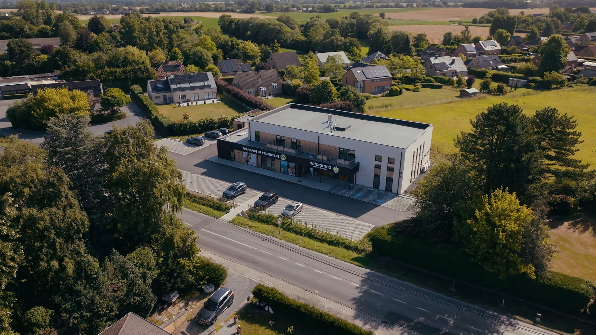 Bâtiment moderne de centre médical et pharmacie entouré de verdure et maisons dans une zone résidentielle.