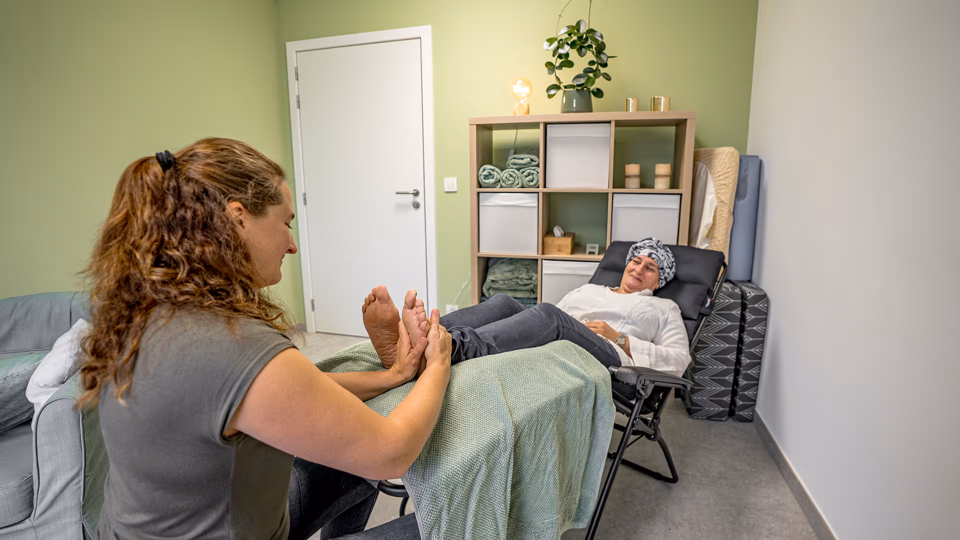 Une femme effectue un massage des pieds sur une autre femme allongée sur une chaise inclinable dans une pièce calme.