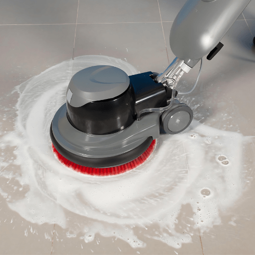 A Yeshua Cleaning employee operates a floor cleaning machine on a tiled floor. The machine scrubs the tiles and grout, leaving a noticeably clean and shiny surface. The employee, focused and efficient, wears the company’s uniform, demonstrating professionalism in maintaining high cleanliness standards.