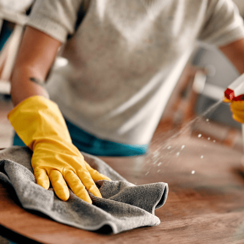Yeshua Cleaning employee holding a spray bottle and cleaning a table with a microfiber cloth.