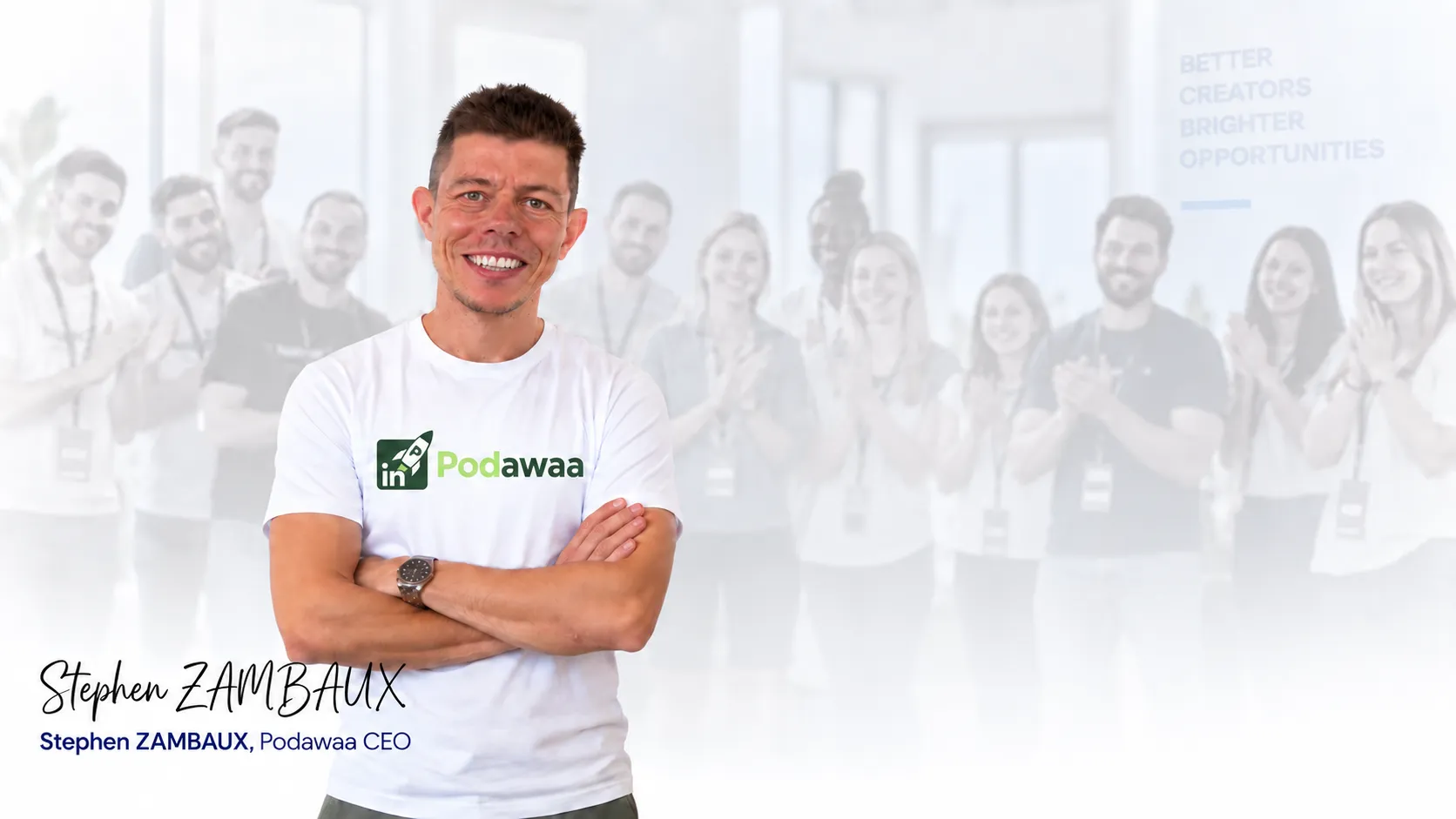 Stephen Zambaux, Podawaa CEO, stands in front with arms crossed wearing a white Podawaa t-shirt, smiling at the camera; a group of people blurred in the background are clapping.