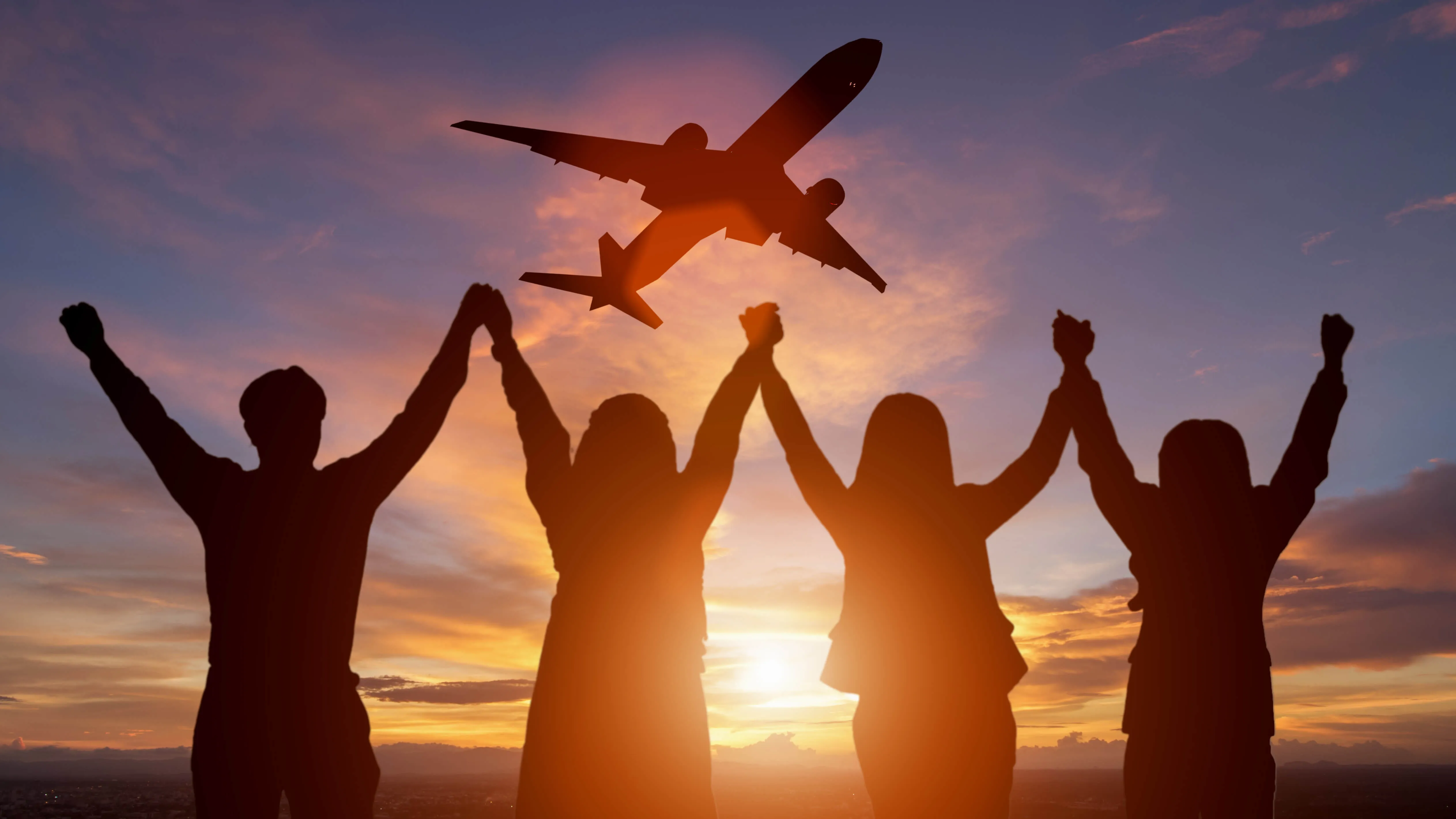 silhouette of group of people holding hands in the air with a plane flying overhead
