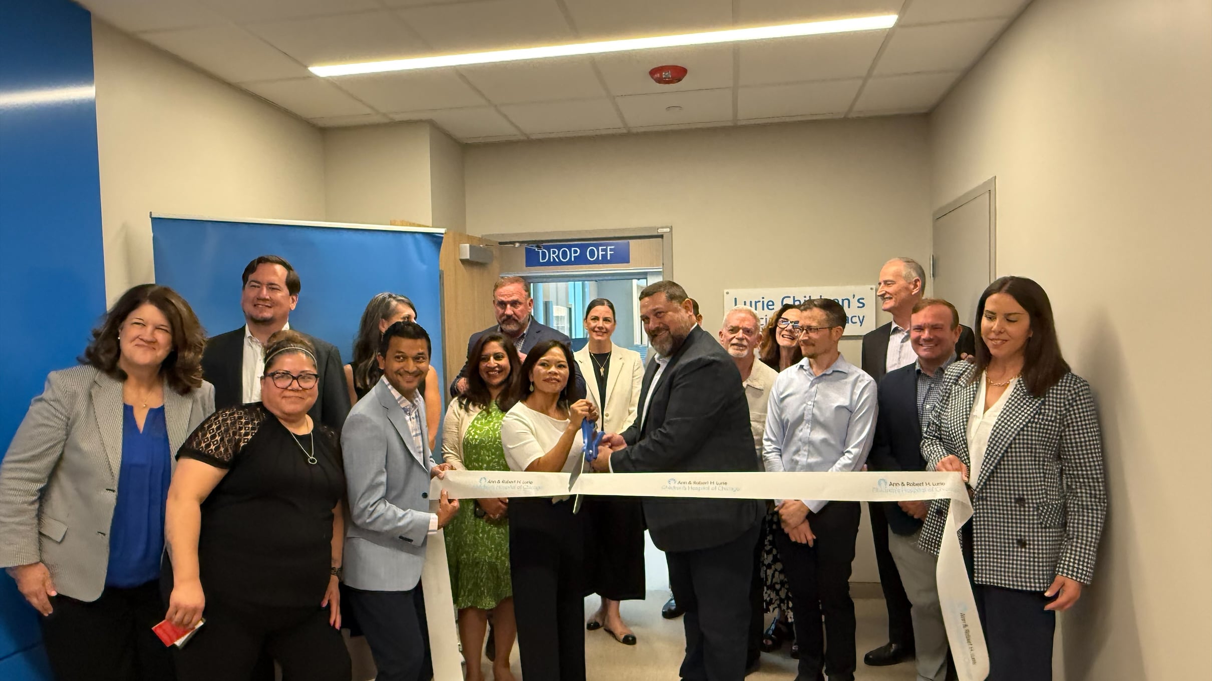 People stand at a ribbon cutting ceremony in front of a pharmacy.