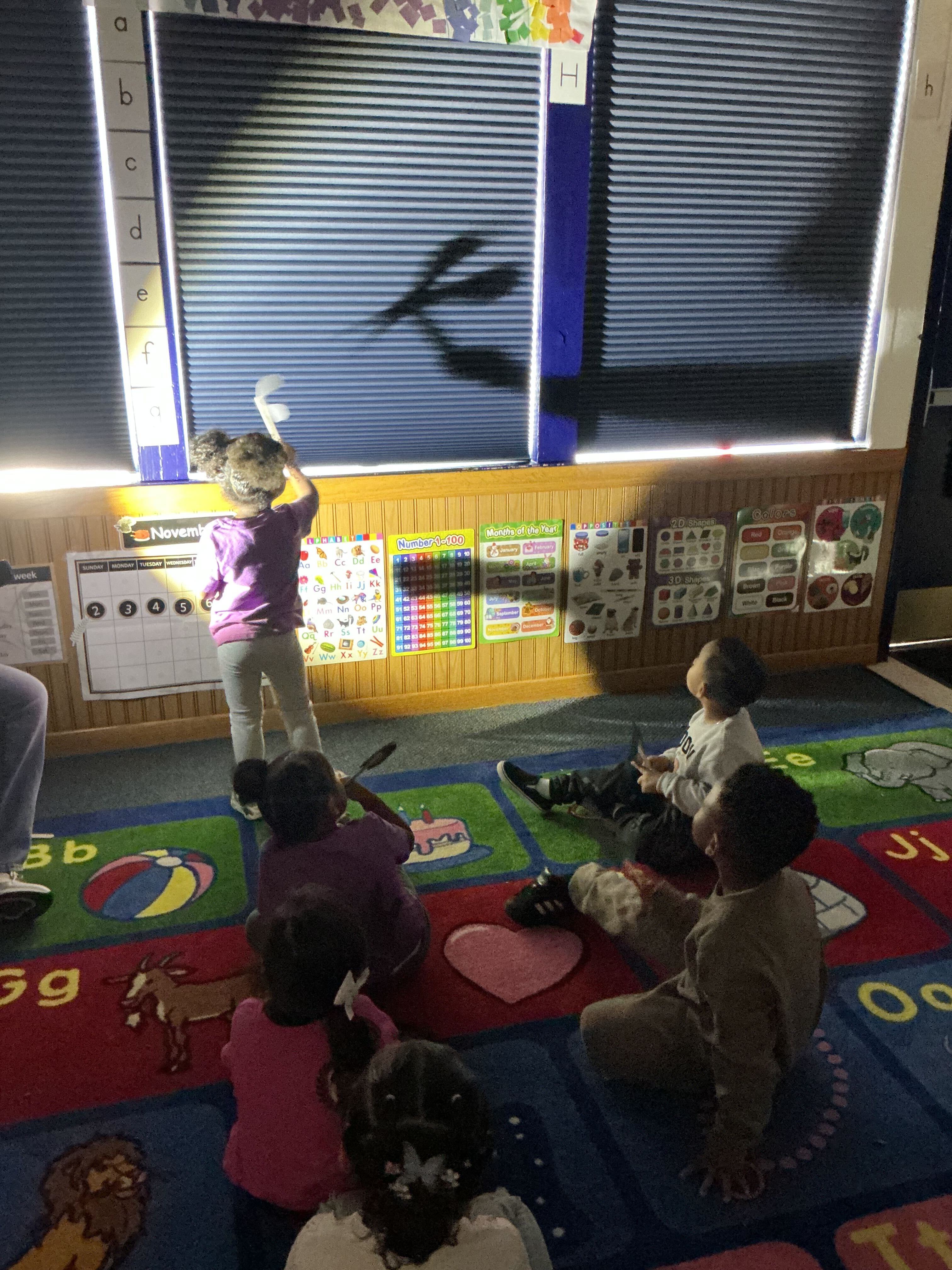 A child writing something on a board in a preschool classroom with other children watching.