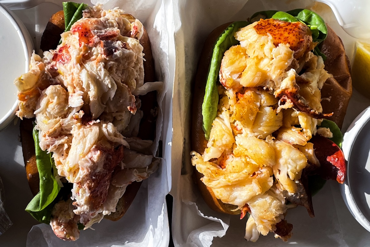 Two lobster rolls - one cold with mayo, the other hot with butter sit side by side to be eaten.