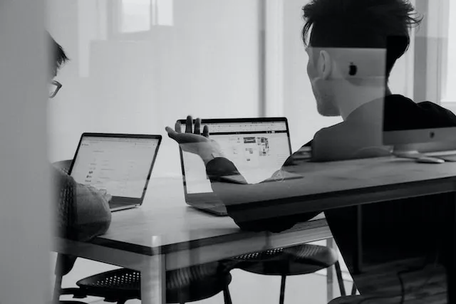 two people sitting at a table with laptops