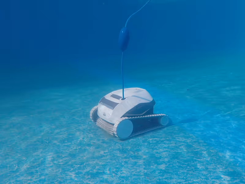 Robotic pool cleaner moving underwater, connected by a floating cable, efficiently cleaning the pool floor.