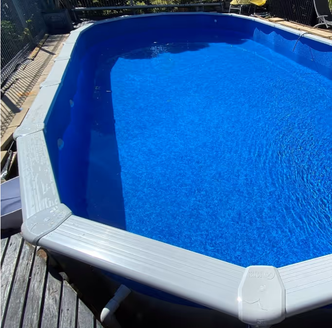 Above view of a clean Driclad Orca Saltwater Pool, blue, above-ground swimming pool with a white frame and wooden deck surrounding it.