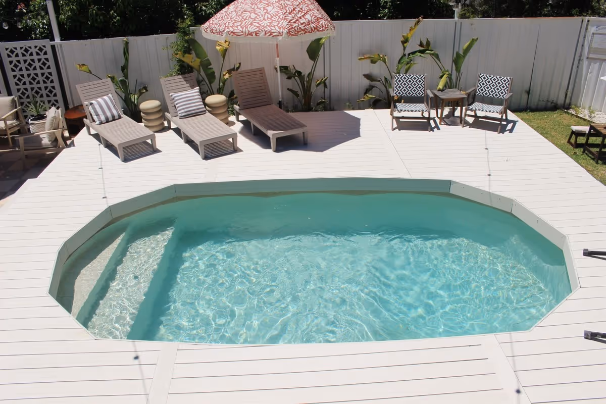 Backyard with an octagonal in-ground pool surrounded by white decking and lounge chairs under an umbrella.