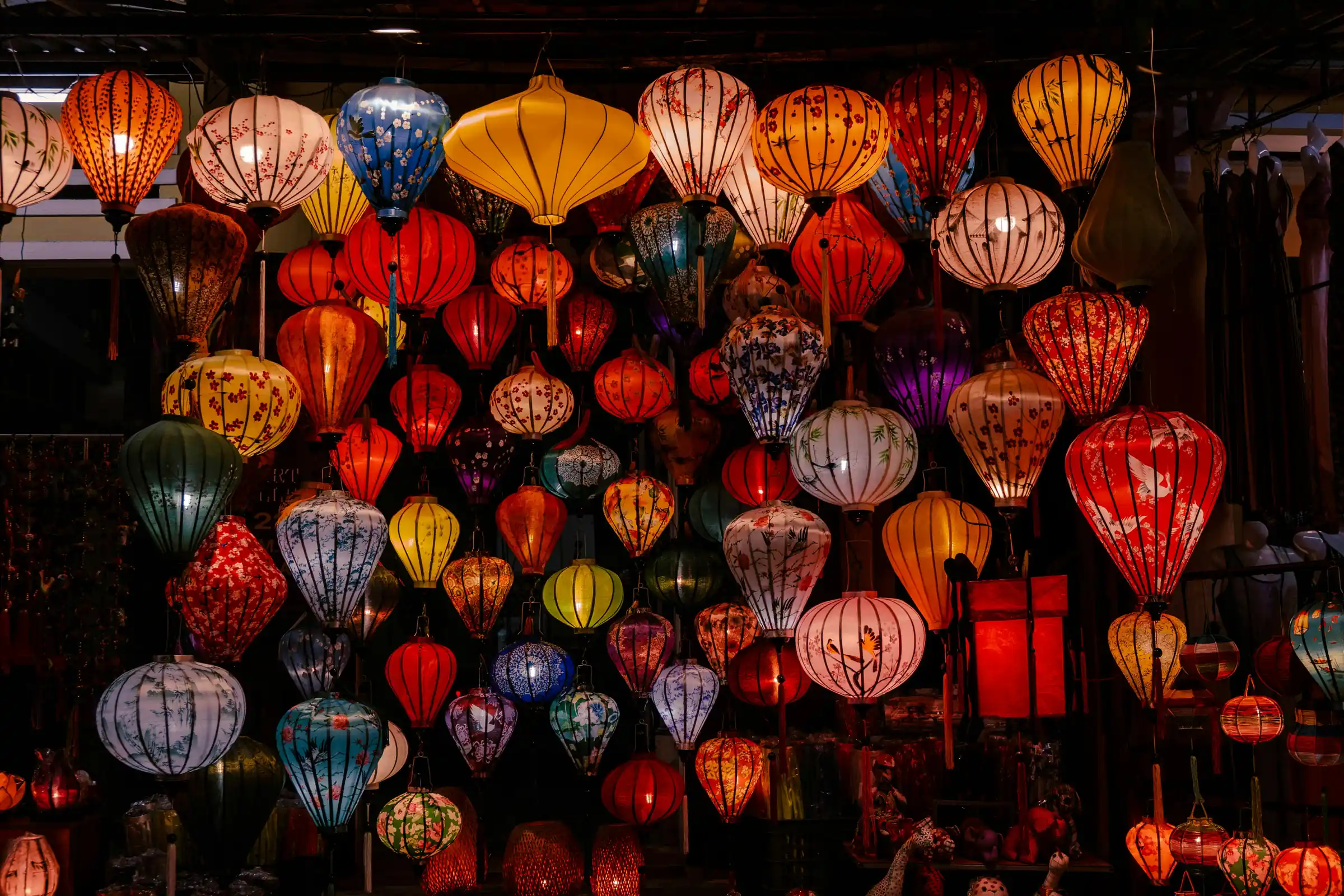 Felinare de matase vietnameze, colorate si aprinse, atarnate intr-un magazin, noaptea. Foto: Sammie Nguyen / Unsplash