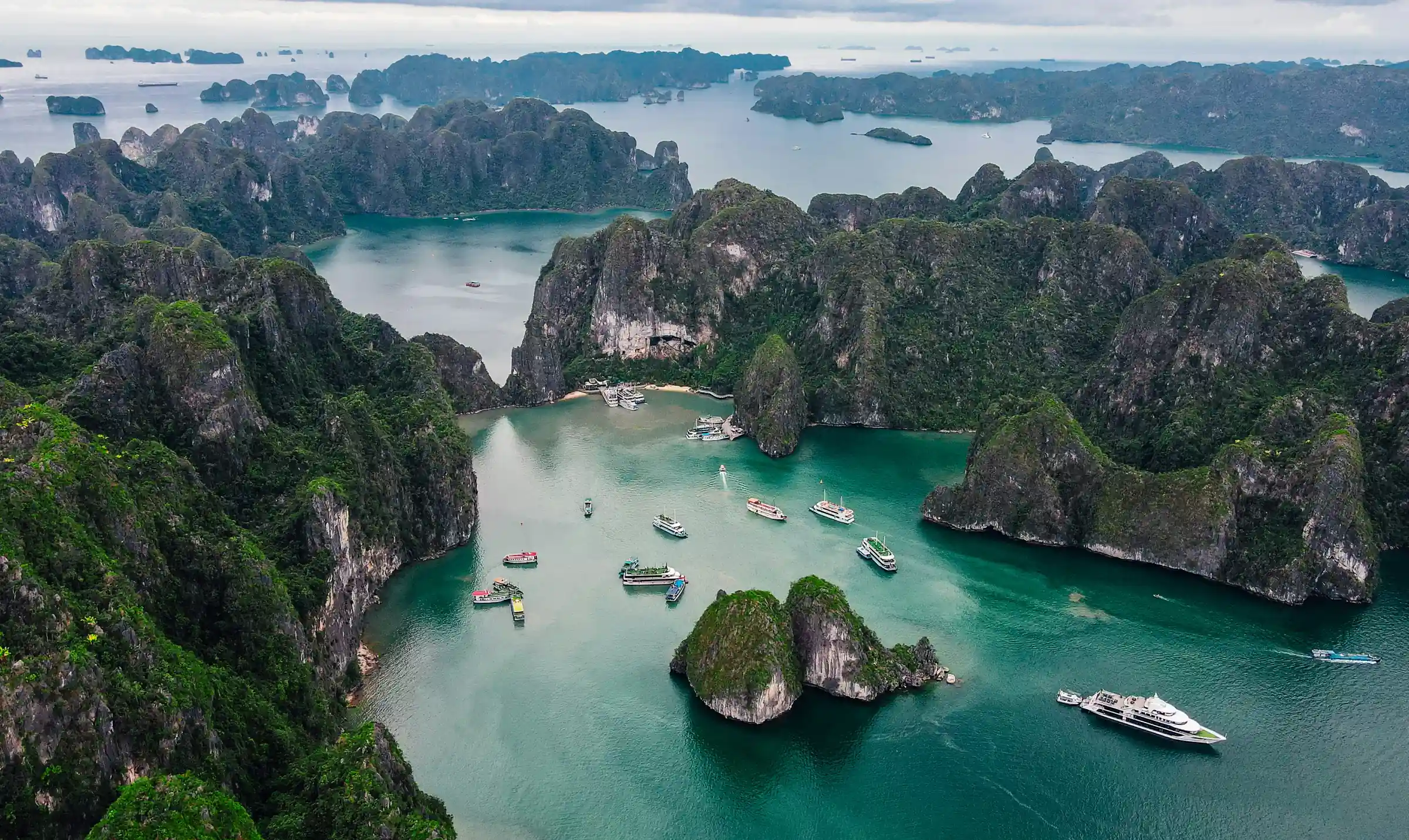 Vedere aeriana a Golfului Ha Long, cu insule calcaroase acoperite de vegetatie si barci de croaziera. Foto: Ryan Le / Unsplash