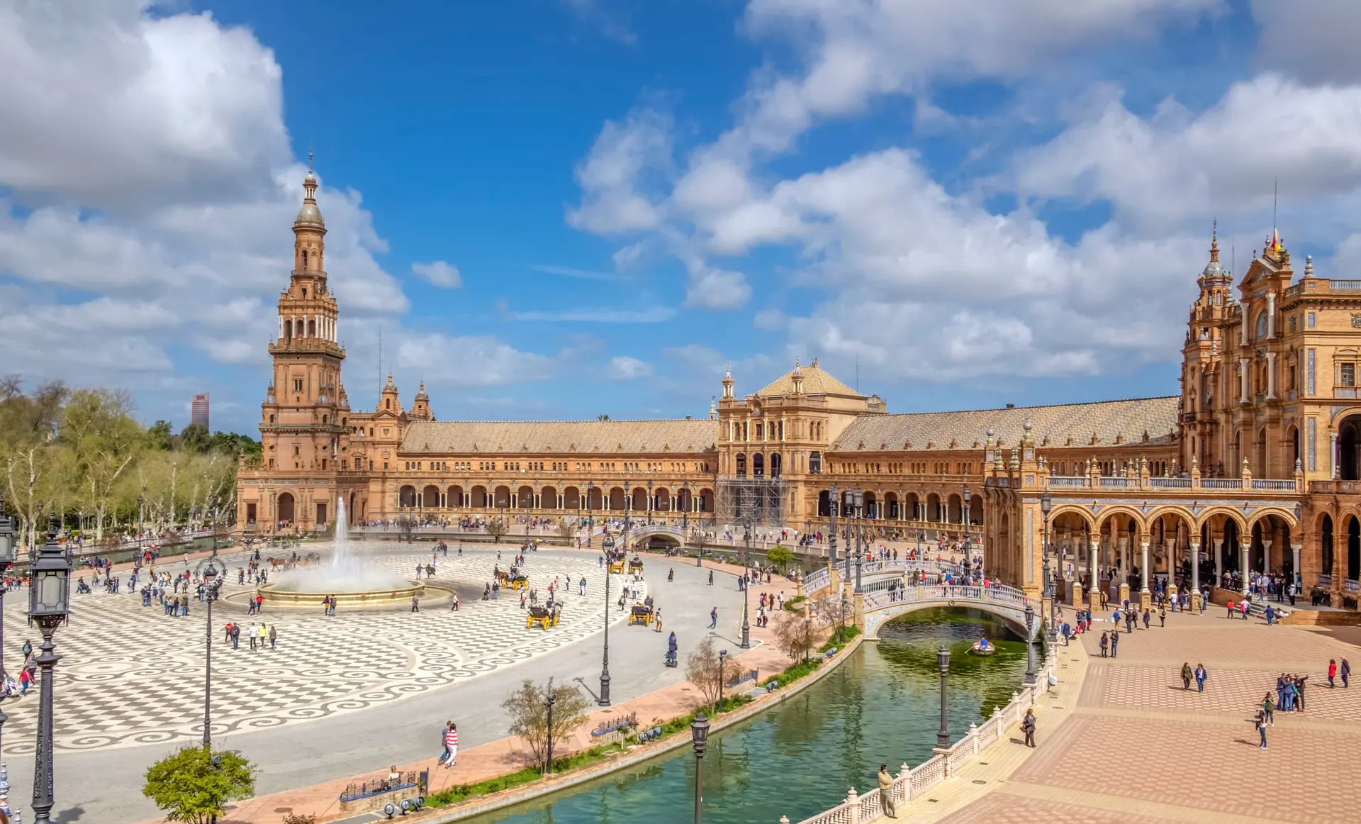 Plaza de Espana din Sevilla vazuta panoramic, cu turisti, trasuri, fantana centrala si canal cu poduri ornamentale. Foto: Bruggi / Pexels