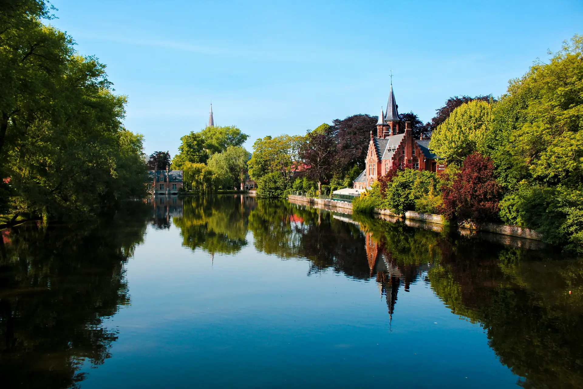 Lacul Minnewater din Bruges cu reflexii ale cladirii medievale din caramida rosie si arbori pe maluri, vara. Foto: Ivo Sousa Martins / Pexels