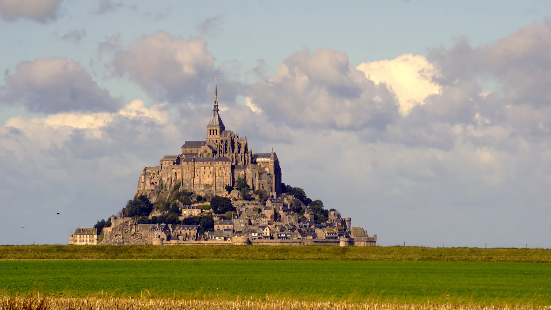 Mont Saint-Michel in Normandia, Franta, vazut de la distanta de pe campurile verzi, sub un cer cu nori. Foto: Pexels