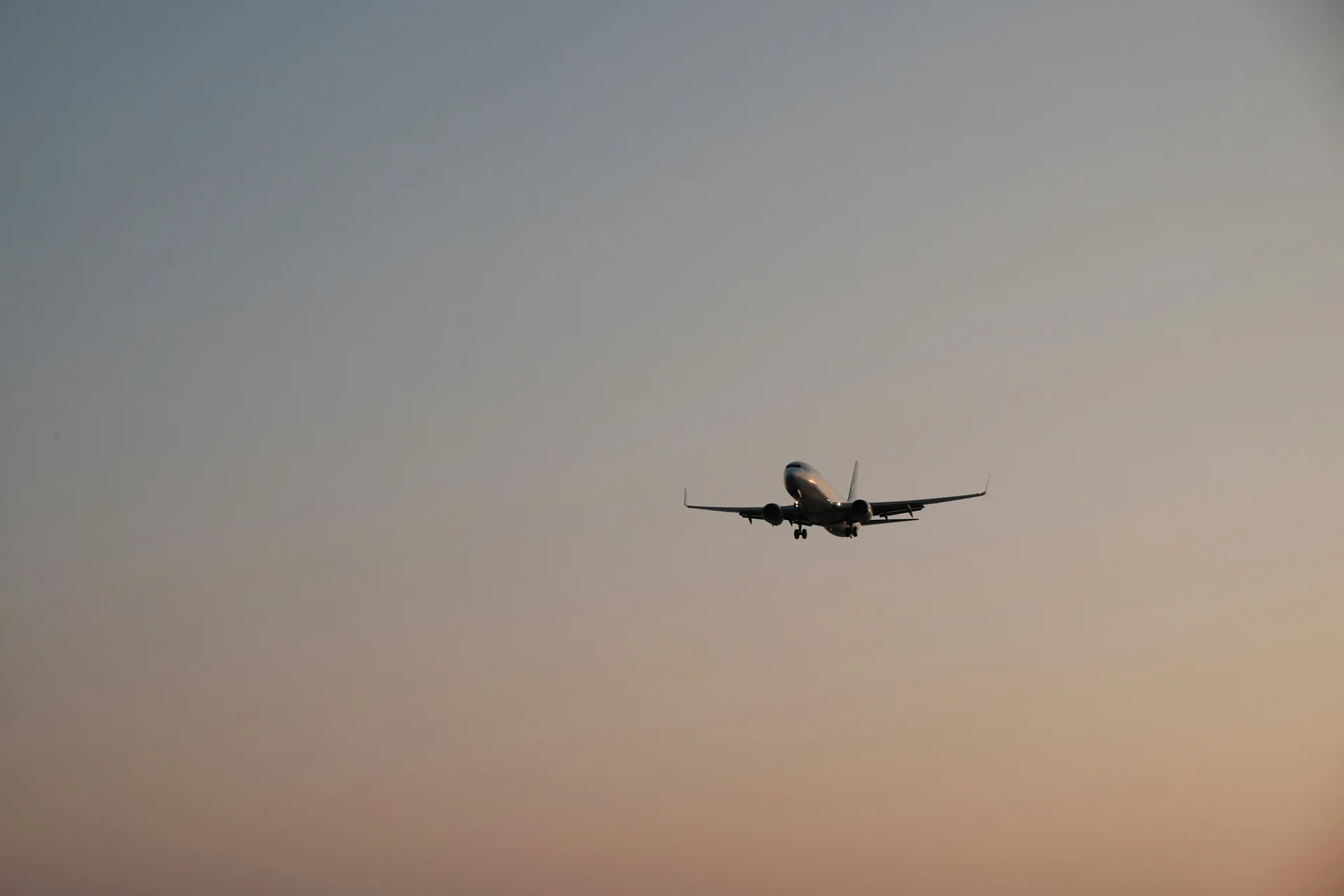 Avion comercial in zbor pe cerul rozaliu la apus, cu trenul de aterizare scos. Foto: Aryanditho Rakasiwi / Unsplash