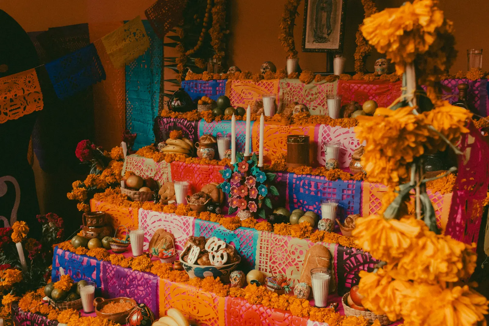 Altar de Día de los Muertos cu craite, papel picado colorat, lumanari, paine, fructe si cranii de zahar. Foto: Chris Luengas / Unsplash