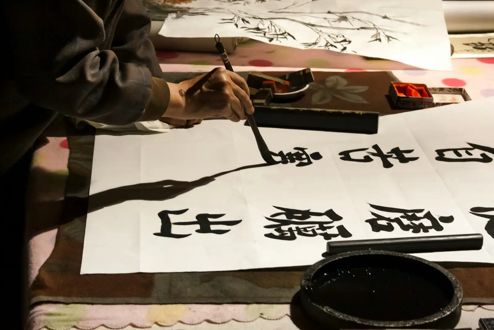 Mana unui caligraf care scrie caractere chinezesti cu pensula si cerneala neagra pe hartie alba. Foto: Marco Zuppone / Unsplash