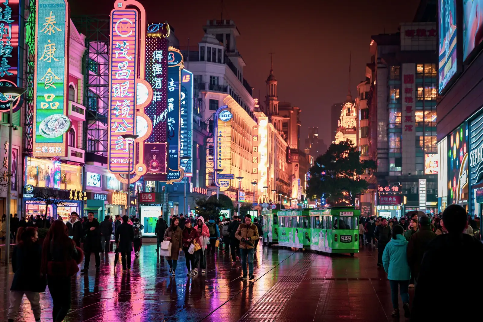 Strada pietonala Nanjing din Shanghai noaptea, cu reclame neon, pavaj ud si un trenulet turistic verde. Foto: Hyunwon Jang / Unsplash