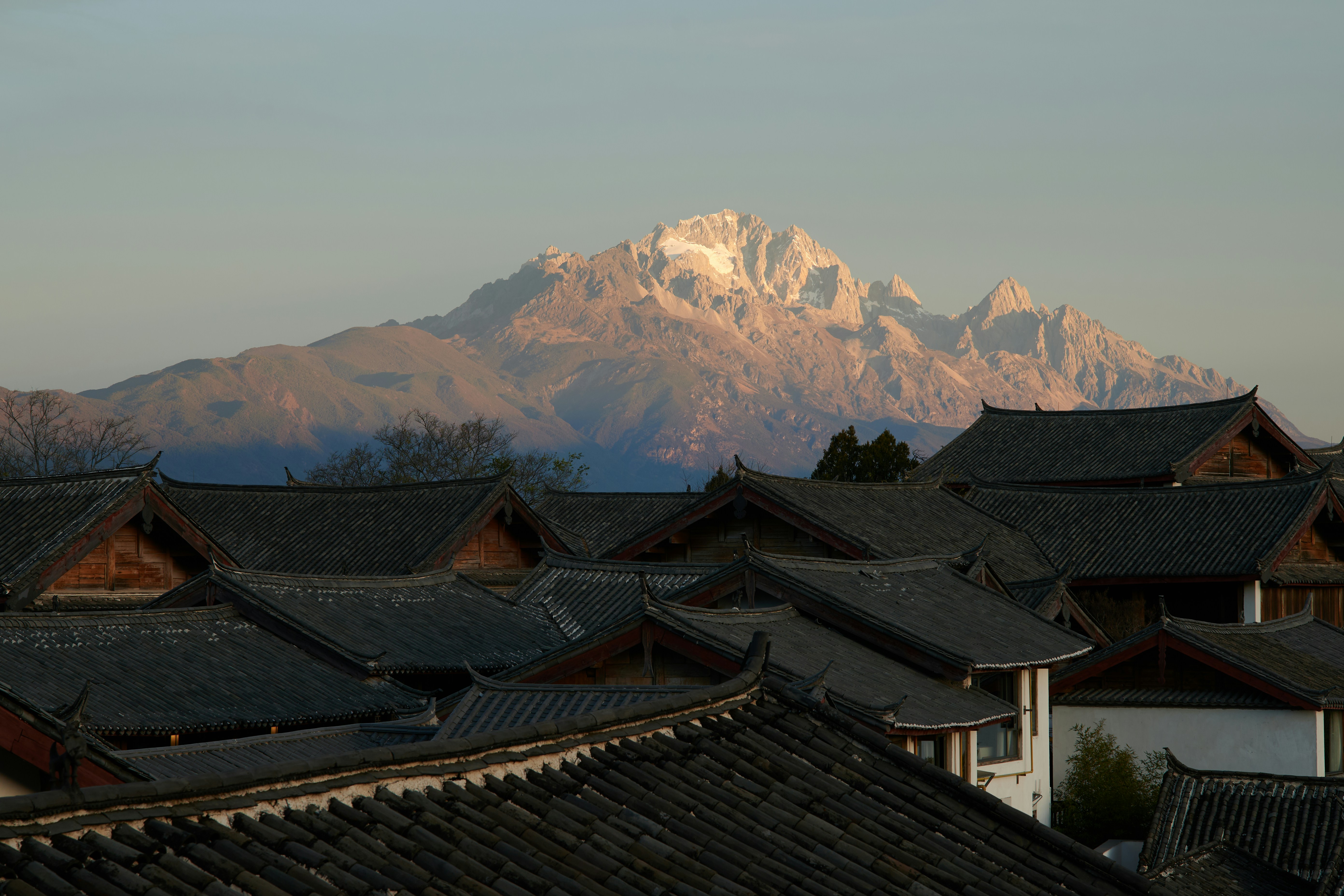 Acoperisurile orasului vechi Lijiang, cu Muntele de Zapada al Dragonului de Jad luminat de soare in fundal. Foto: Pic Kaca / Unsplash