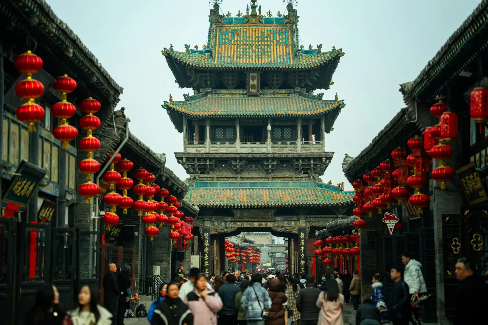 Turnul Pietei din orasul vechi Pingyao, cu acoperis din tigla smaltuita, vazut de pe o strada cu lampioane rosii. Foto: Shane Lopez / Unsplash
