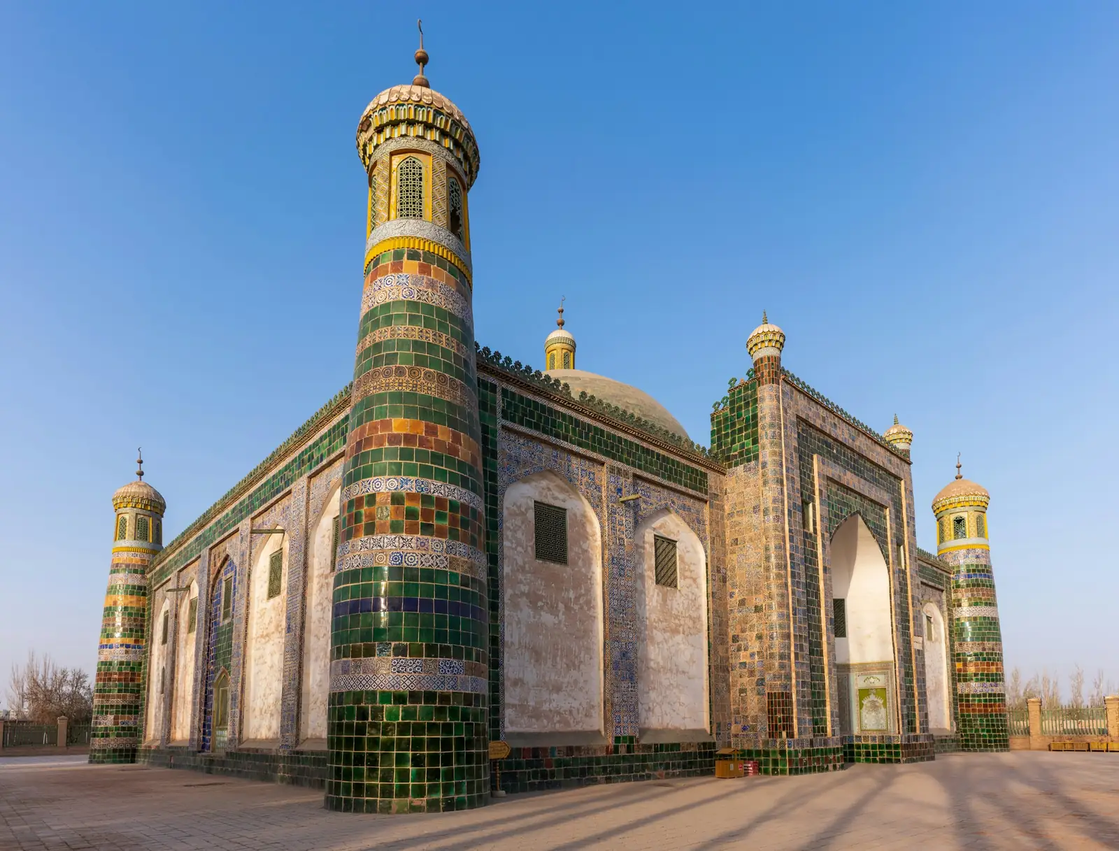 Mausoleul Afaq Khoja din Kashgar, cu minarete si ziduri placate cu faianta verde si albastra, sub cer senin. Foto: Pix Tresa / Unsplash