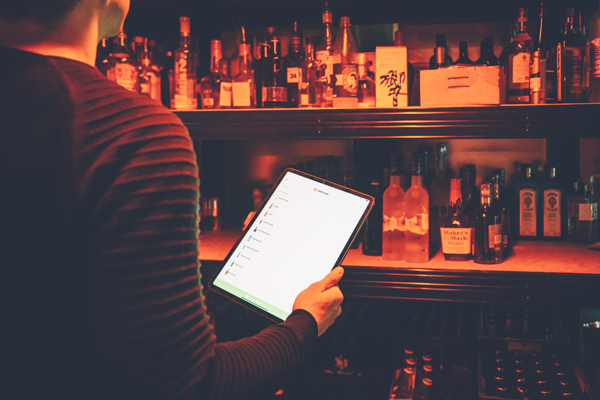Barkeeper nutzt Tablet zur digitalen Bestandsaufnahme von Spirituosen in einer Bar.