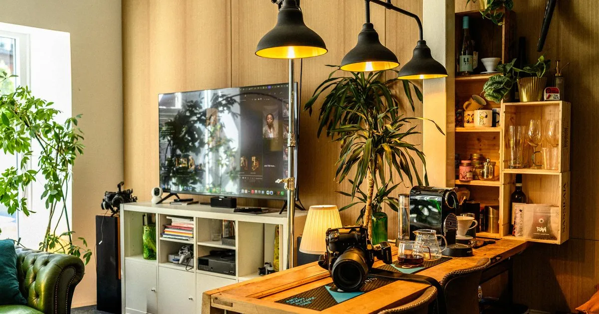 Cozy room with a TV on white shelves, camera on wooden bar counter, and plants under warm hanging lights.