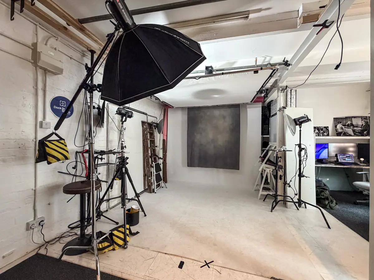 Photography studio with lighting equipment, gray backdrop, and a small office area with computers.
