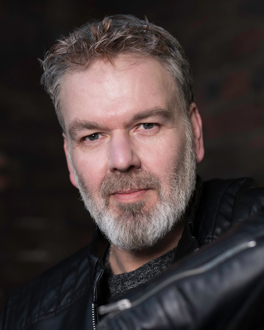 Studio headshot of a man in a leather jacket, chin forward and eyes on the lens, photographed at Dock Street Studio in Leeds