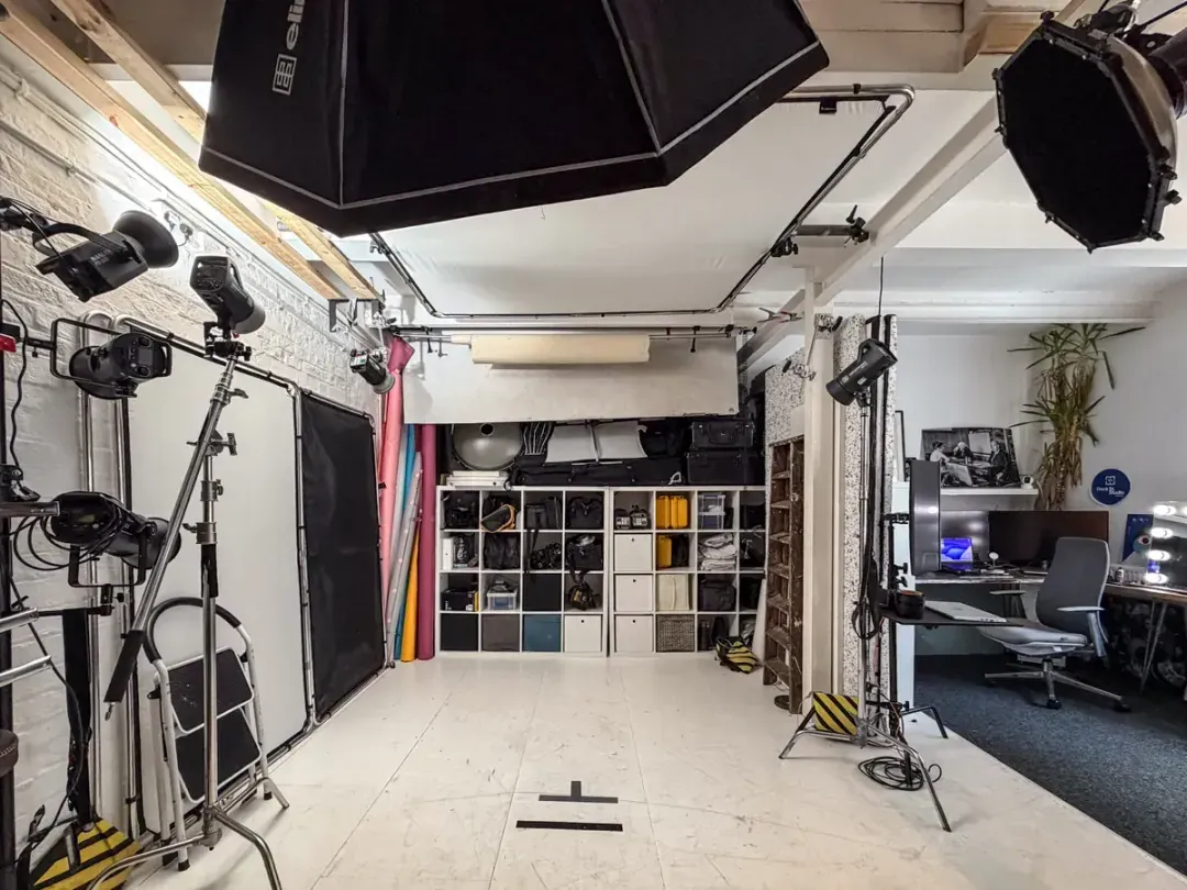 Inside Dock Street Studio’s photography and video space in central Leeds: overhead softboxes on a ceiling rig, studio strobes on stands, coloured paper backdrops, a labelled kit store and the edit suite at the back